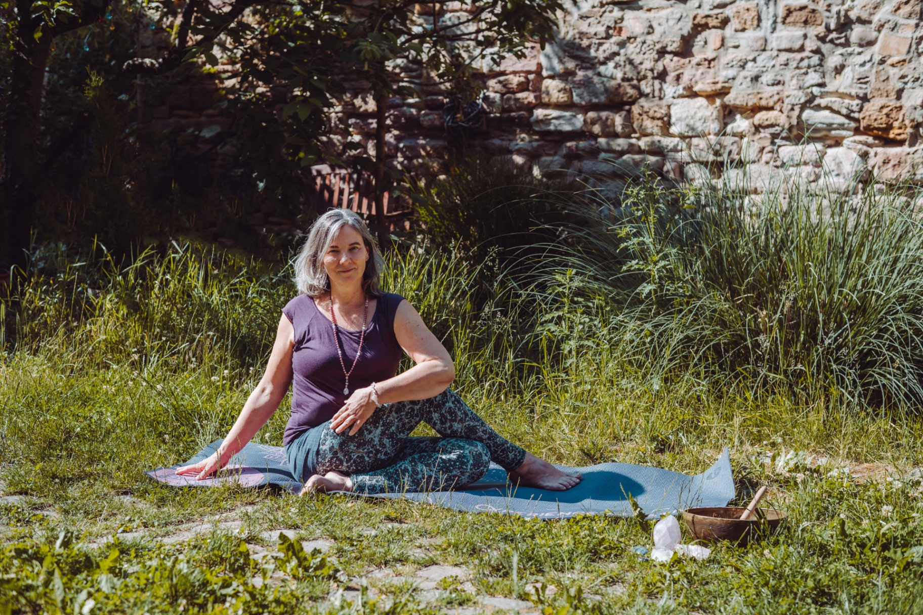 Susanne in einer Yoga-Drehhaltung auf der Matte im Grünen